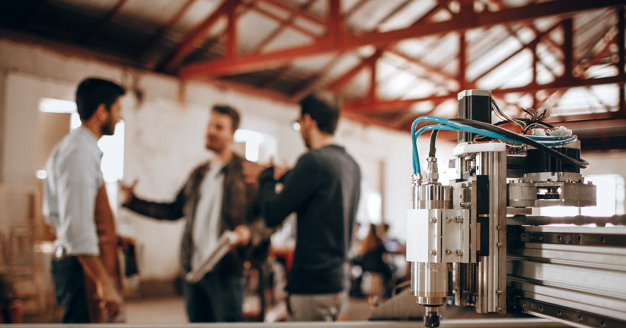 Eine Person steht in einer Werkhalle neben einer großen Maschine und führt eine ergonomische Analyse durch. Im Hintergrund sind industrielle Arbeitsbereiche sichtbar.