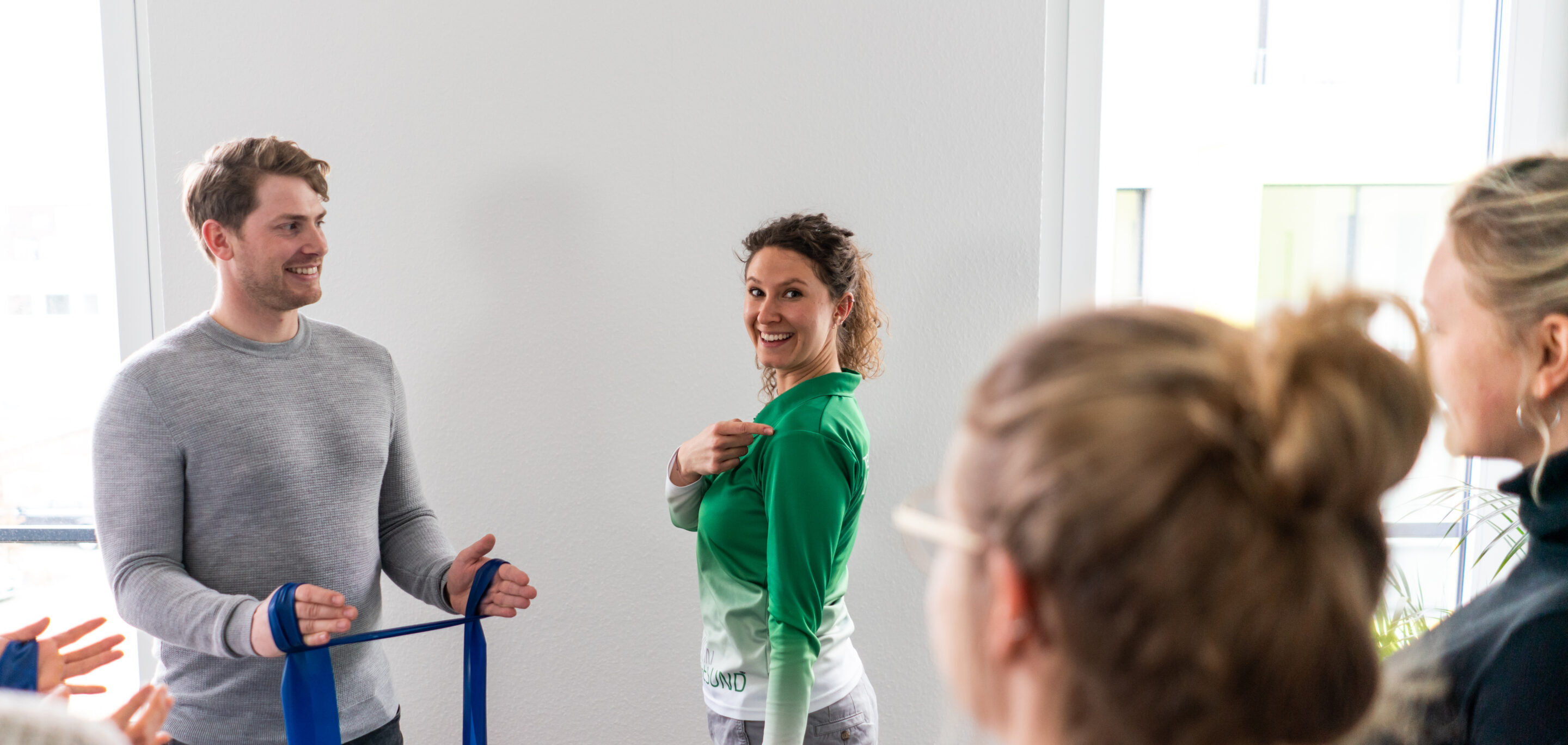 Eine Person zeigt einer Gruppe eine Übung oder ein Hilfsmittel zur Entlastung von Schulter- und Nackenbereich. Die Teilnehmenden stehen in einem hellen Seminarraum.