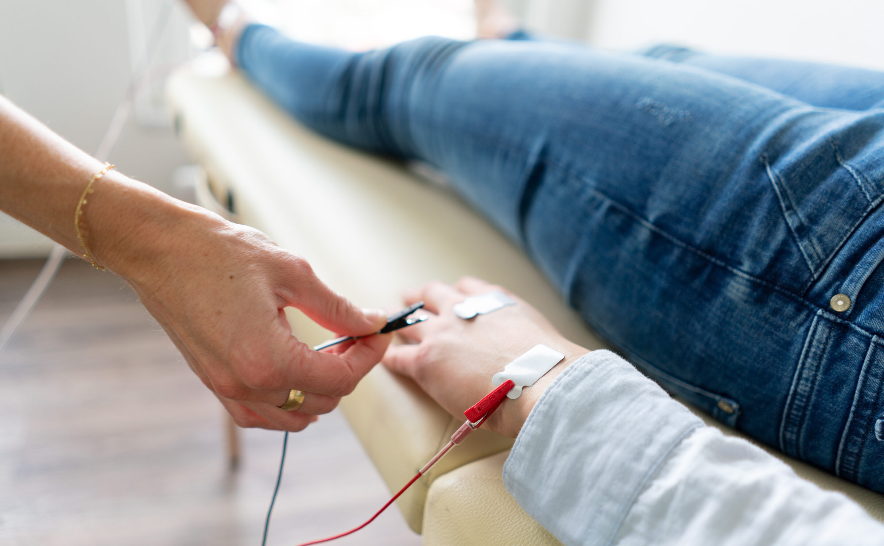 BIA-Messung Eine Hand legt Elektroden an den Unterarm einer liegenden Person an, als Teil einer gesundheitsbezogenen Messung oder Behandlung.